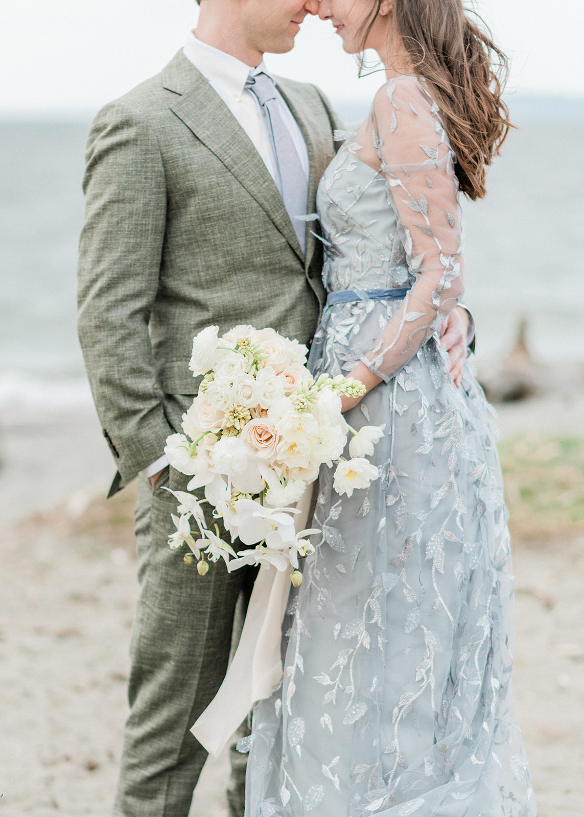 Couple holding white orchid bouquet with blush ribbon in wind