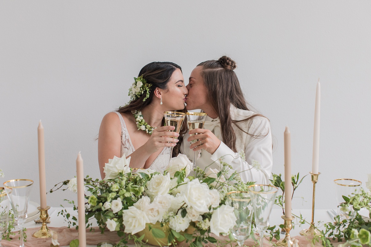 Modern-White-Wedding-Kiss-Toast Brides kissing while toasting their champagne glasses