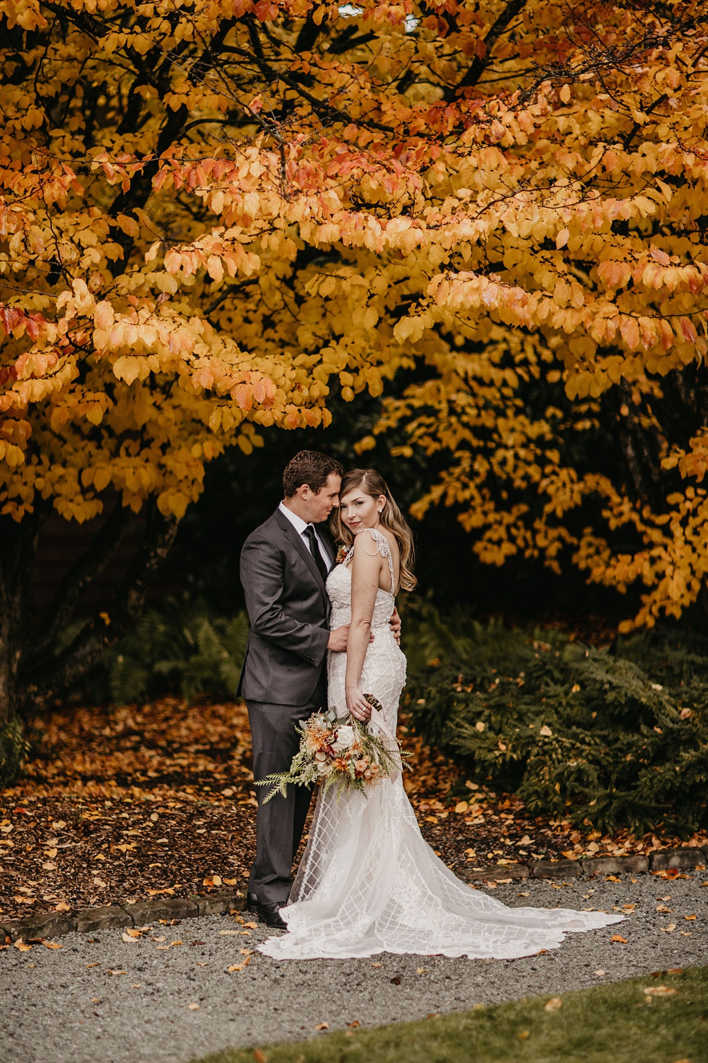 a bride and groom standing under a tree with bright yellow fall leaves