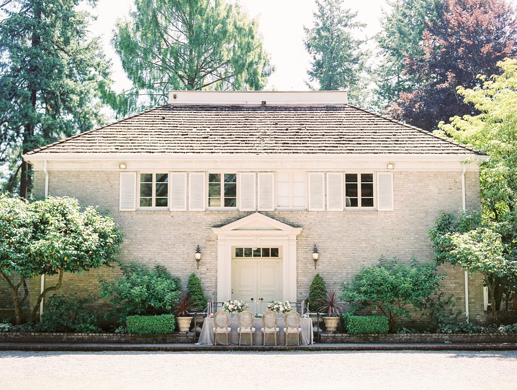 A large house (Lakewold Gardens) with a table set for a wedding in front of it