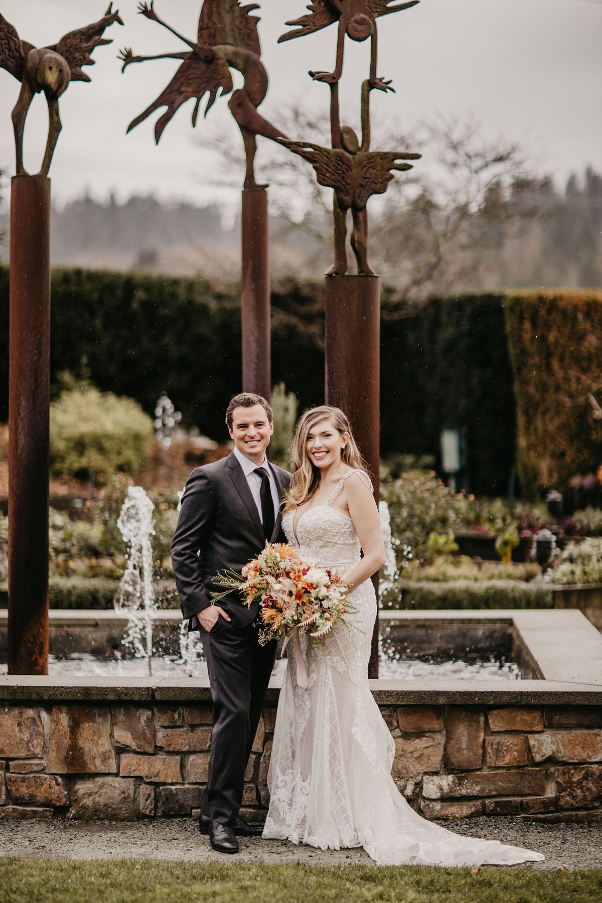 the bride and froom standing and smiling in front of a garden fountain at the Willows Lodge