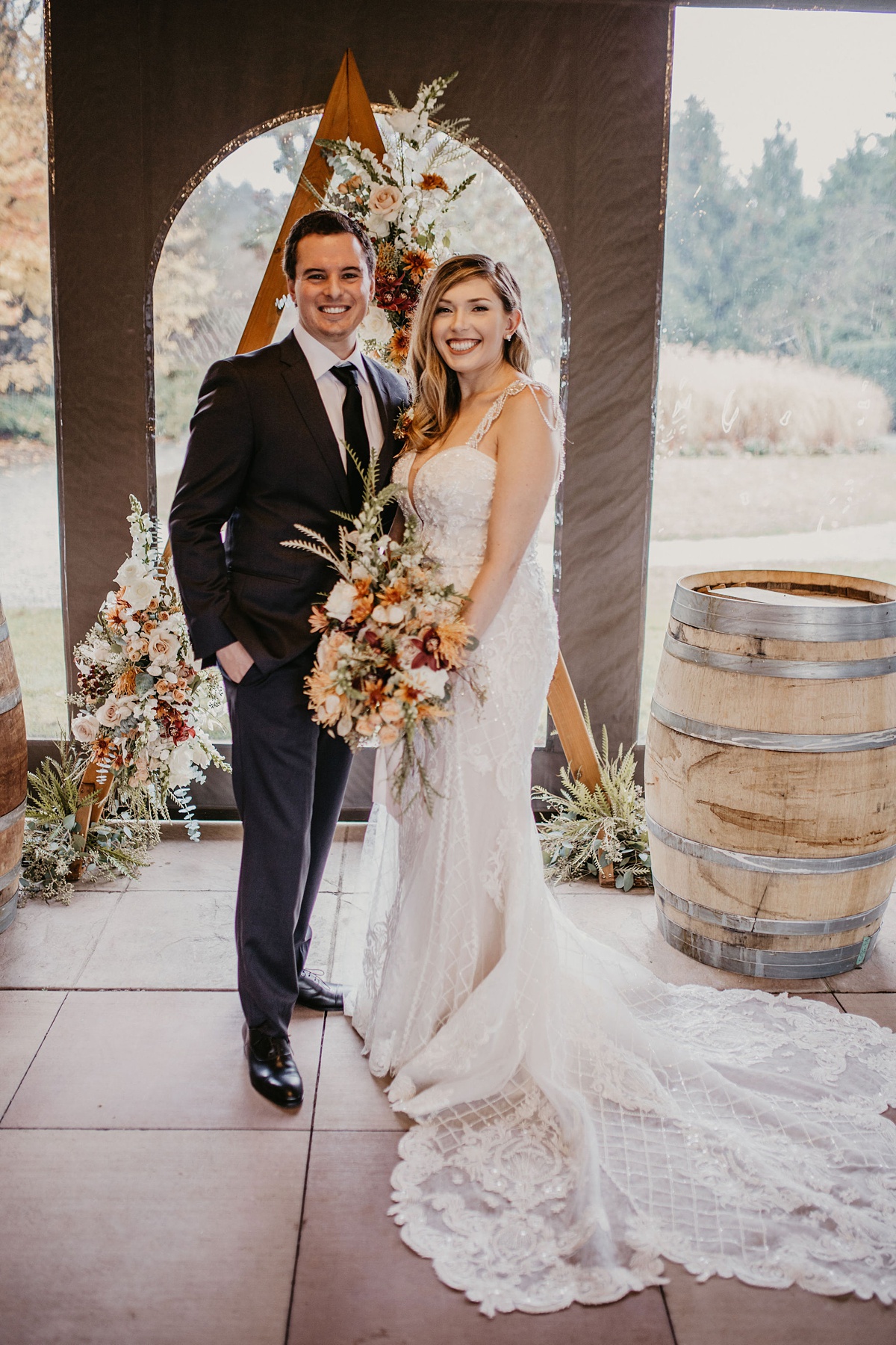 the bride and groom standing in front of their floral arch, with the bride holding her bouquet
