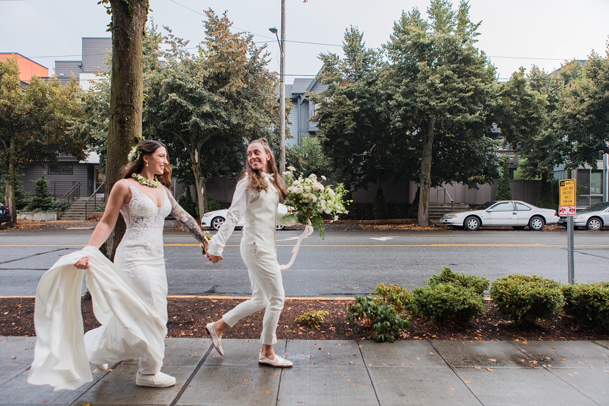 Modern-White-Wedding-Couple-Running-Outside-With-Bouquet A lesbian couple celebrates their white wedding with a quick run down the sidewalk together
