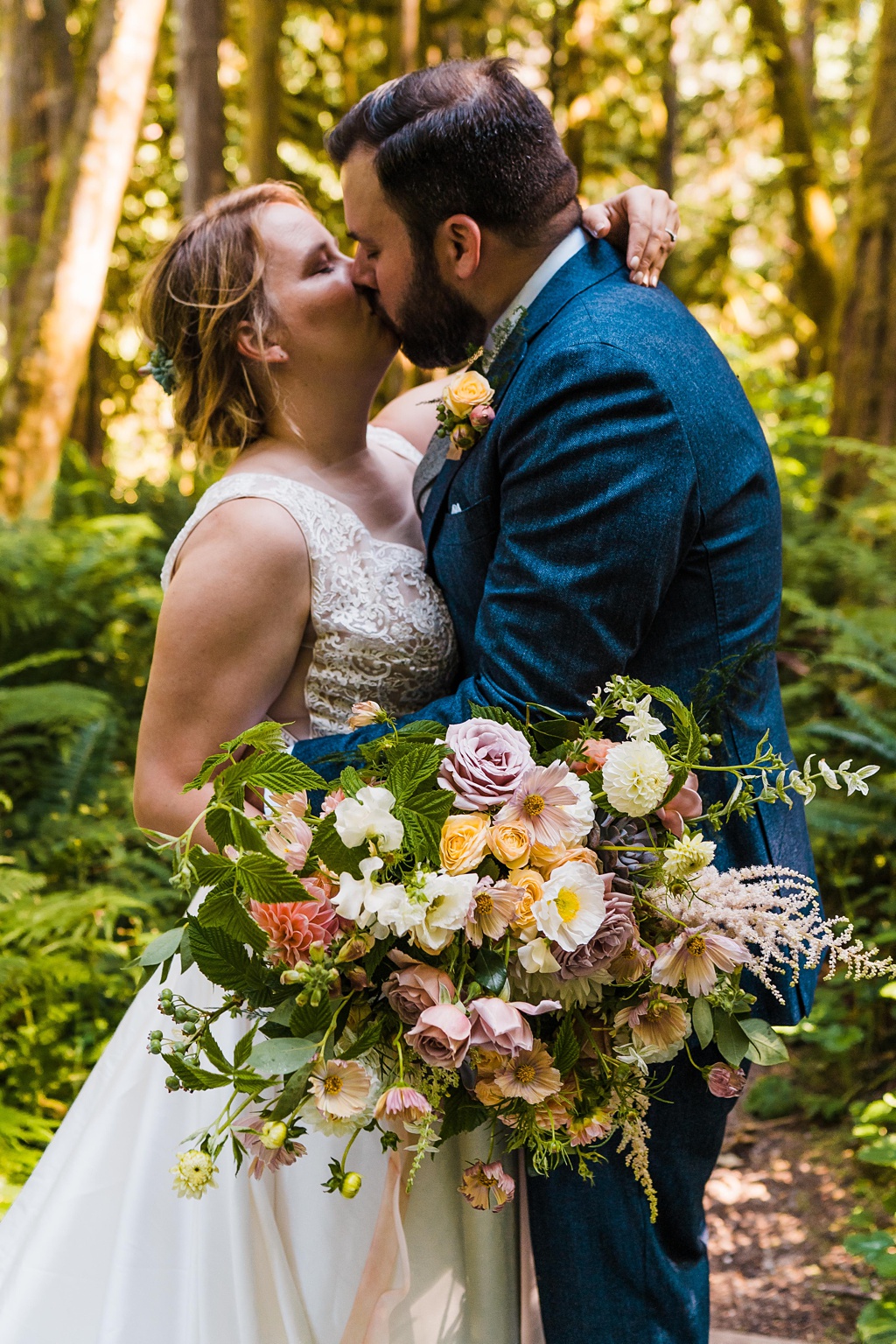 Mountain-Wedding-with-Vibrant-Summer-Blooms-Bridal-Bouquet A bride and groom kiss in the woods holding a bouquet
