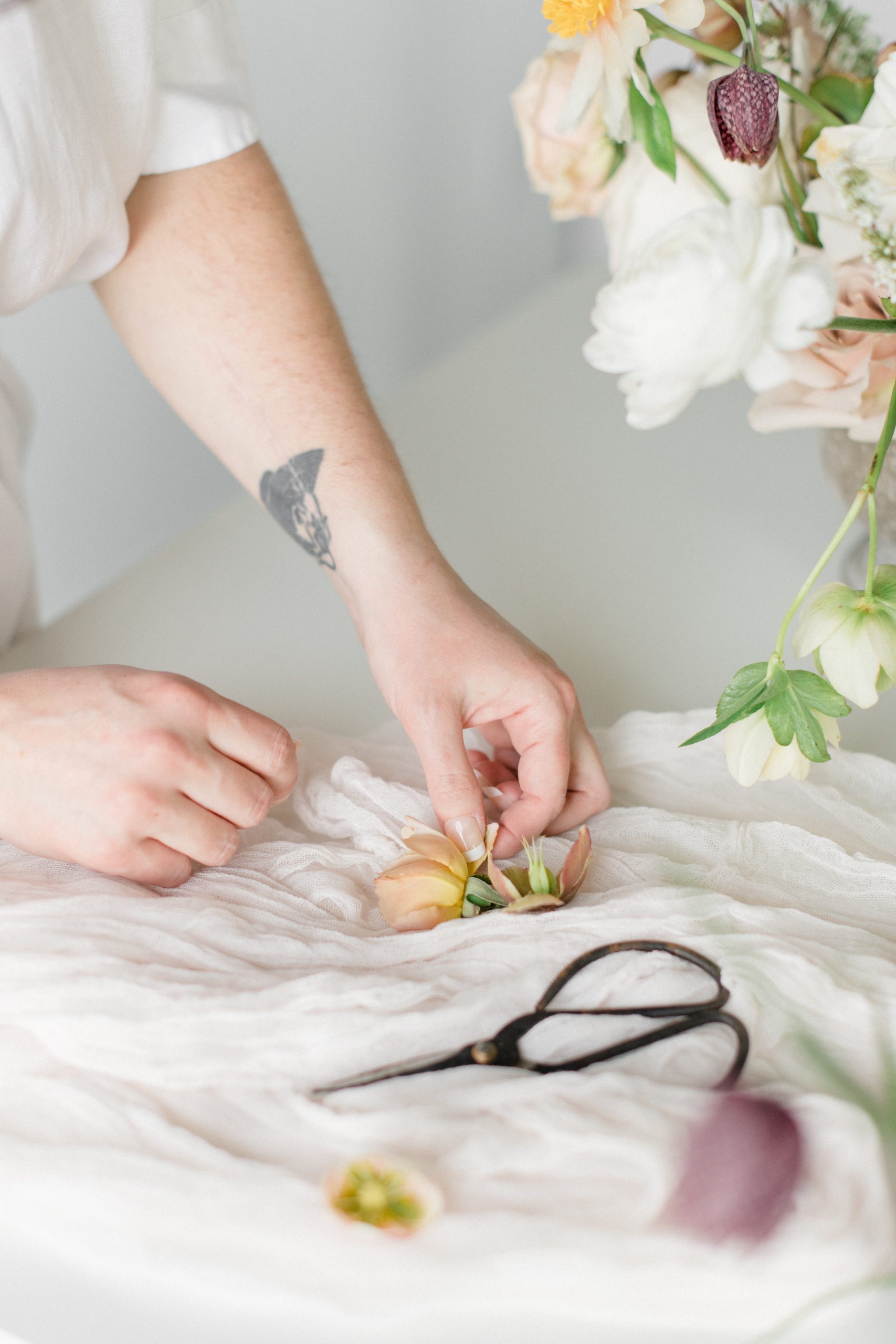 A shot of florist Carolyn Kulb's hands arranging blooms on a gauzy table runner with snips