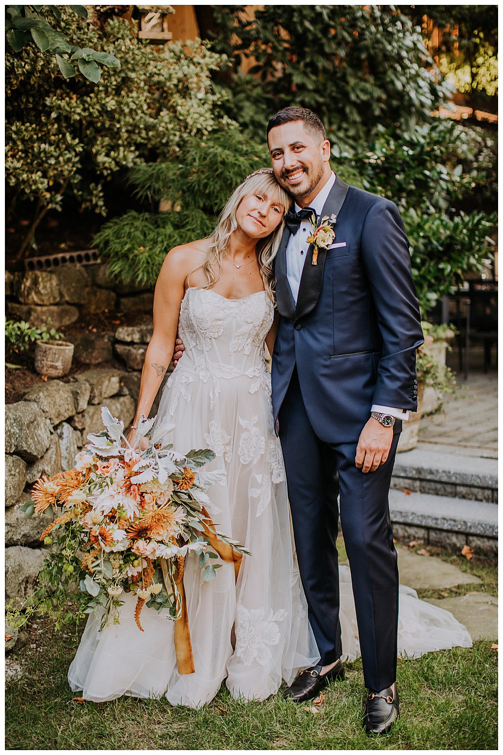 The couple posing, close to each other, with the bride holding the bouquet