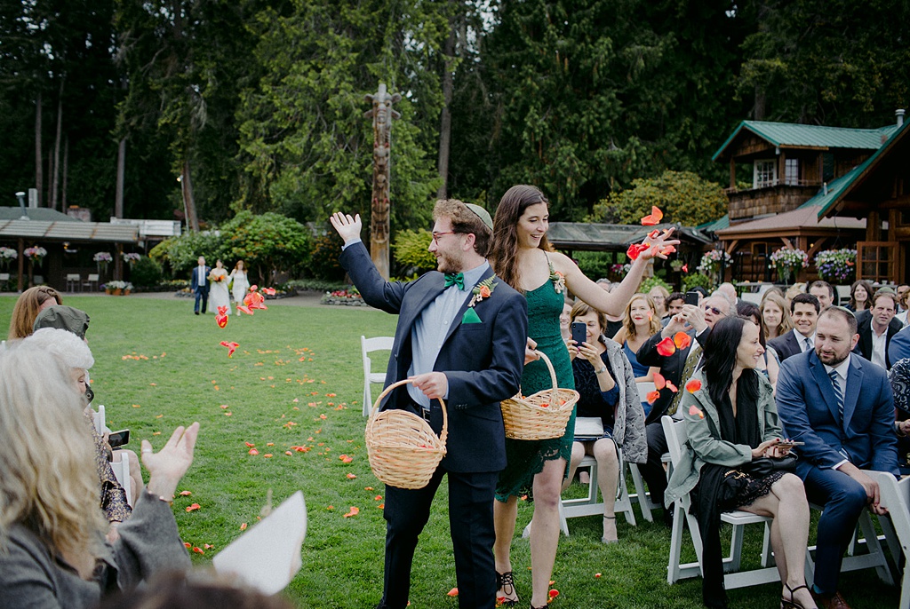 Adult "flower girls" throw petals in the wedding aisle at Kiana Lodge
