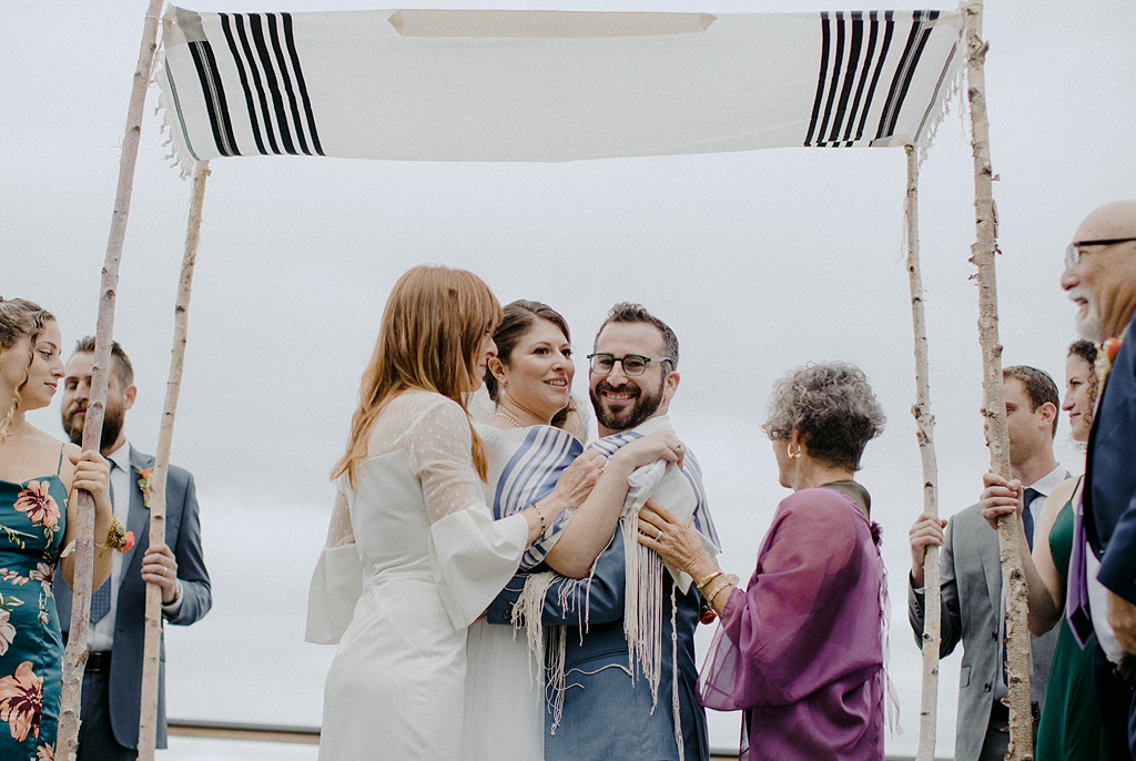 The couple embraced by both of their mothers during the Jewish wedding ceremony at Kiana Lodge